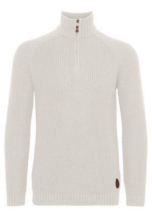 Kremfarget strikkegenser med høy krage, halv-glidelås foran, ribbestrikkede mansjetter og et brunt logopatch på nederste del.