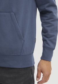 Felpa blu navy con tasca a marsupio, polsini e orlo a coste. Tessuto morbido e dettagli di cucitura visibili. Etichetta della taglia sul lato della cucitura.