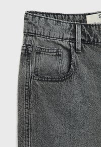 Gros plan sur un jean en denim noir lavé montrant la ceinture, la boucle de ceinture, la poche avant et une partie de la couture latérale.
