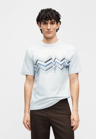 Ανοιχτό μπλε βαμβακερό μπλουζάκι με γεωμετρικό σχέδιο ζιγκ-ζαγκ σε γκρι, μαύρο και μπλε. Κοντά μανίκια και λαιμόκοψη γύρω από το λαιμό.