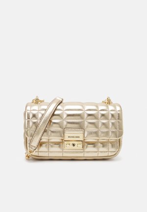Złota pikowana torba na ramię Michael Kors ze skóry, z klapką i regulowanym paskiem na ramię na białym tle.