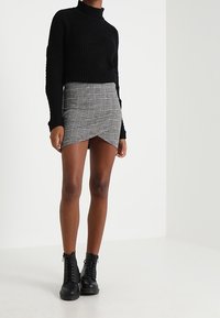 Pull en maille noir à col roulé, jupe mini à carreaux gris avec ourlet asymétrique, et bottines noires à lacets.