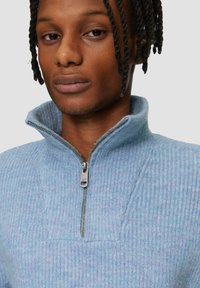 Hellblauer, gerippter Pullover mit hohem Kragen und einem viertel Reißverschluss, versehen mit einem silbernen Reißverschluss und weichem Material.
