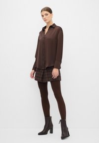 Camisa marrón de botón, falda de cuadros, medias marrones, botas altas de tacón marrones. Tela suave, diseño estructurado, patrones sutiles.