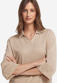 Beige polo shirt met korte mouwen, een V-hals en een relaxte pasvorm. Zachte textuur en minimale stikseldetails, geschikt voor casual wear.
