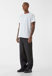 T-shirt bianco in cotone oversize abbinato a pantaloni in denim scuro. L'outfit presenta un design semplice e minimale, senza fantasie.