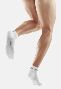 White athletic socks with a textured sole, ribbed cuff, and mesh details for breathability. Features a zigzag pattern on the bottom.