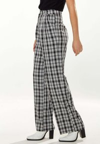 Black and white plaid high-waisted trousers with a wide-leg cut, featuring a smooth texture and sleek silhouette, paired with white ankle boots.
