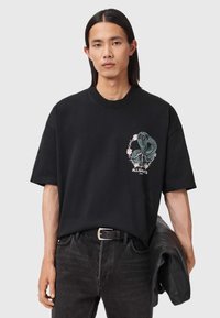 Μαύρο βαμβακερό T-shirt με γραφικό φίδι και λουλούδια, στρογγυλή λαιμόκοψη, άνετη εφαρμογή, συνδυασμένο με σκούρα τζιν και μαύρο μπουφάν.