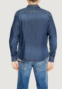 Camicia in denim blu scuro, con colletto, polsini con bottoni e dettaglio sulla spalla. Abbinata a jeans in denim blu chiaro con cuciture distintive.