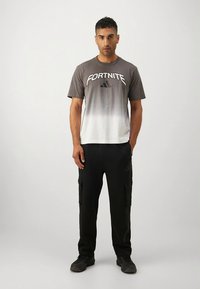 Pilkas ir baltas marškinėlių gradientas su "FORTNITE" užrašu, derinamas su juodomis cargo kelnėmis su šoninėmis kišenėmis ir laisvo kirpimo.