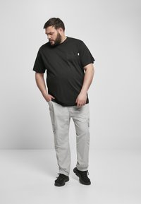 Schwarzes Baumwoll-T-Shirt mit einer Brusttasche, kombiniert mit hellgrauen Cargo-Hosen mit Seitentaschen und schwarzen Sneakers.