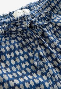 Tissu à motifs bleus et blancs avec une ceinture élastique et un cordon en tissu noué, étiquette du vêtement partiellement visible.
