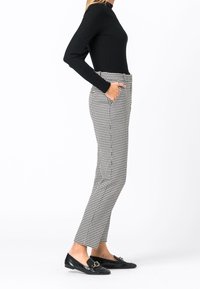 Top a maniche lunghe a righe nere abbinato a pantaloni a vita alta con motivo a scacchi bianco e nero. I pantaloni presentano tasche laterali.