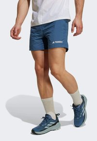 Blå idrottsshorts med TERREX-logotyp, kombinerade med blå och grå sneakers samt krämfärgade ankelsockor. Slät tyg, skräddarsydd passform, medelhöjd.