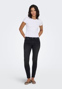 White ribbed short-sleeve top with scalloped edges paired with black skinny jeans. The outfit is complemented by brown ballet flats.