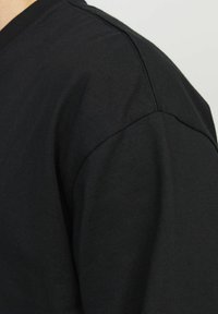 Svart bomulls T-shirt med korta ärmar, med en enkel rund halsringning och mjuk textur. Närbild som betonar axelsömmen.