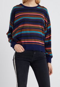 Knitted pullover, navy base with horizontal stripes in red, orange, green, and blue. Long sleeves, relaxed fit, and a crew neckline.