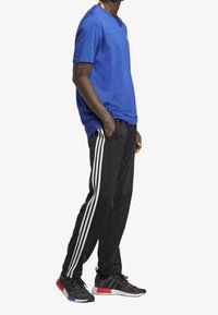 Camiseta de algodón azul, pantalones deportivos negros con tres rayas blancas y zapatillas negras con acentos rojos y azules. Conjunto de ropa activa casual.