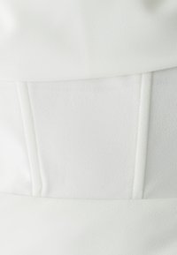 Primo piano di un tessuto bianco con texture e dettagli di cucitura verticali su un indumento strutturato.