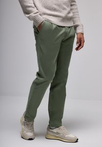 Green cotton trousers with a relaxed fit. Worn with light gray sneakers. Sweater is light gray with ribbed cuffs.