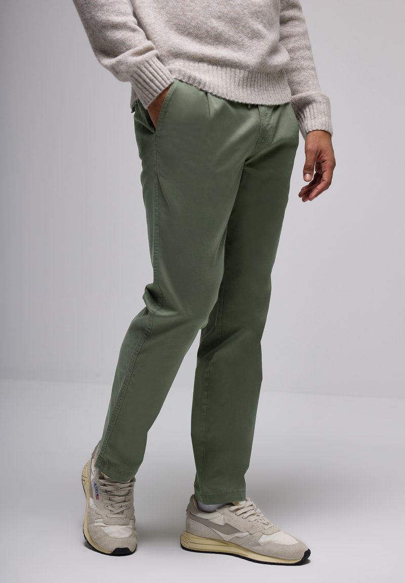 Green cotton trousers with a relaxed fit. Worn with light gray sneakers. Sweater is light gray with ribbed cuffs.