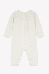 White knitted romper with long sleeves, textured pattern, and tiny heart motifs. Features snap closures at the bottom for easy dressing.