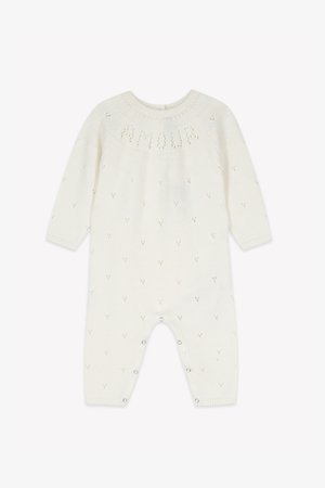 Biały dzianinowy romper z długimi rękawami, wzorem teksturowym oraz małymi motywami serduszek. Posiada zatrzaski na dole, ułatwiające ubieranie.