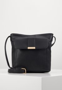 Czarna skórzana torebka na ramię z klapką, złotymi ozdobami i regulowanym paskiem. Gładka faktura, minimalistyczny design, kwadratowy kształt.