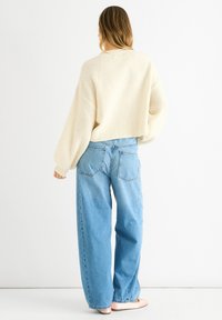 Cream-colored, chunky knit sweater with balloon sleeves, paired with loose, light blue jeans with a high waist and back pockets.