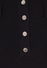 Maglione nero a coste con una chiusura a bottoni dotata di bottoni argentati; tessuto liscio con coste verticali e senza motivi o dettagli.