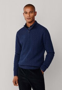 Granatowy sweter w splot żakardowy z ćwierć zamkiem, długimi rękawami i prążkowanymi mankietami. Miękka tekstura, z małym logo na klatce piersiowej.