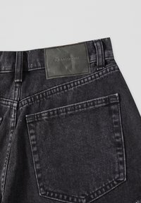 Black denim jeans with a leather label. Features include a high waist, back pockets, and visible stitching details.
