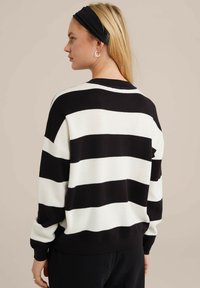 Mustrite ja valge triibuline sviiter, millel on lõdva istuvuse, pehme tekstuur ja ümar kaelus. Varrukad on veidi kitsendatud ja soonikuga mansetid.