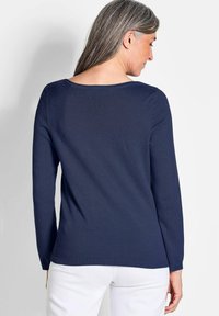Navyblaues Langarmshirt mit rundem Ausschnitt. Stricktextur mit geradem Saum und gerippten Bündchen. Getragen mit weißen Hosen.
