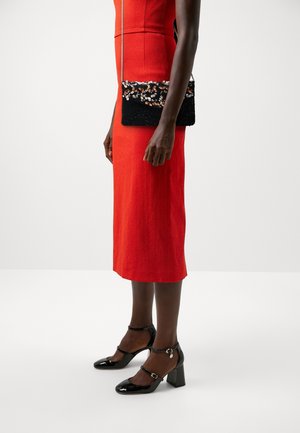 Robe sans manches rouge avec un corsage ajusté et une jupe jusqu'aux genoux, portée avec une pochette noire à paillettes ornée d'accents colorés et des escarpins en vernis noir.