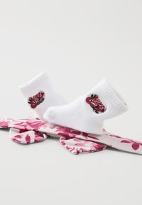Meias brancas de algodão com punhos canelados, apresentando um logótipo da Nike em flores rosas, dispostas sobre um tecido estampado rosa e branco.