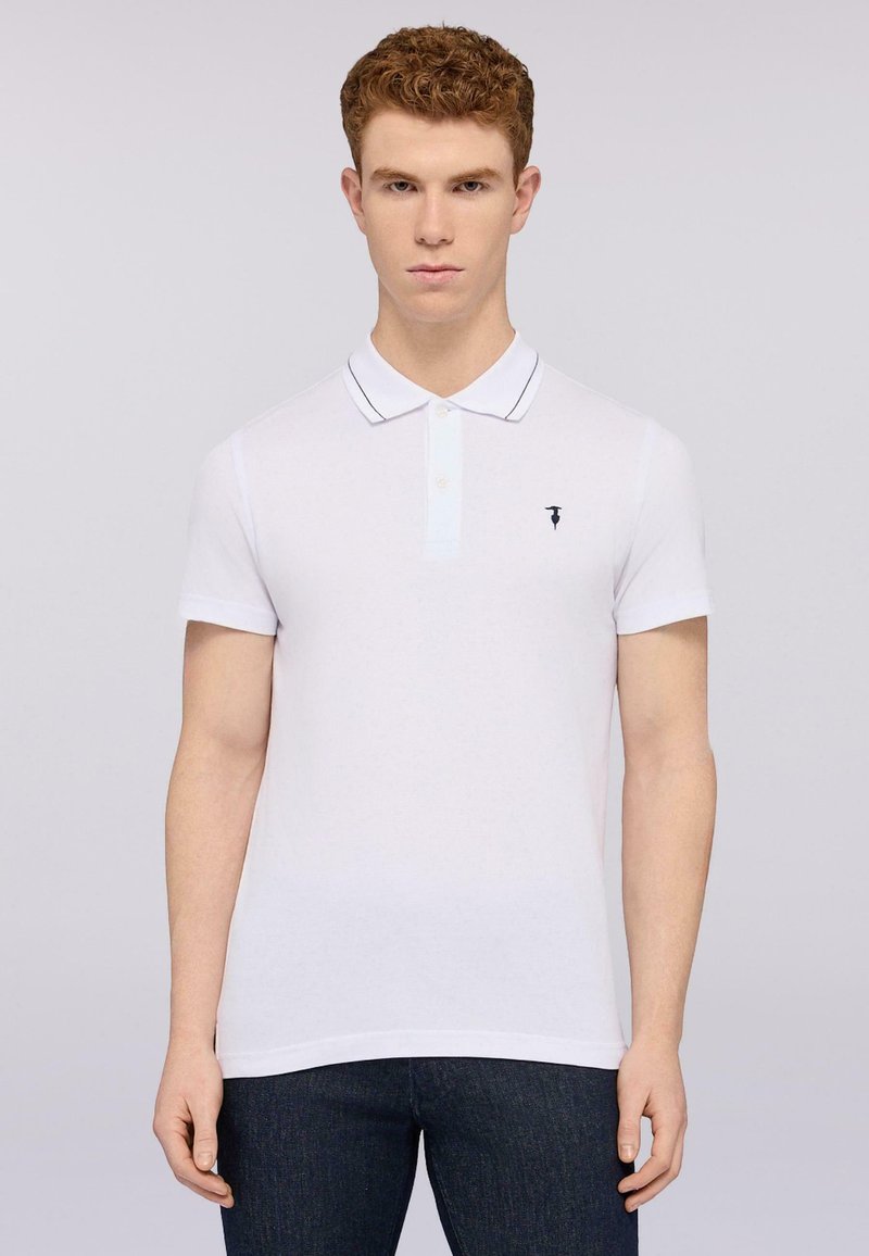 Bílá polokošile s krátkým rukávem, dvoubarevné zapínání na knoflíky, modré akcenty podél límce a malé logo na levé části hrudníku.