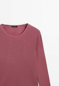 Pull à manches longues, en rib avec une couleur rose poudré, doté d'un col rond et d'une texture douce. Présente une étiquette de marque noire sur le col.