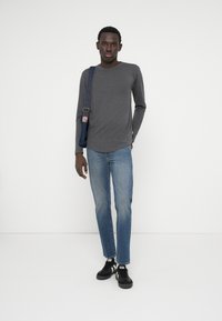 Duga majica s dugim rukavima u sivoj boji, svijetloplave traperice, crne tenisice i torbica preko tijela. Jednostavan dizajn, ležerna fit i mekana tekstura.