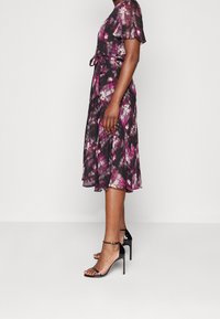 Svart och lila blommig midi-klänning med fladdrande ärmar, midjeband och en flödande kjol. Bärs med svarta stilettklackar.