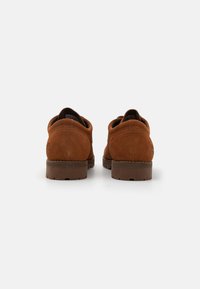 Des chaussures en daim marron avec une forme arrondie, dotées d'une finition texturée, d'une semelle en caoutchouc marron solide et de coutures décoratives au niveau du talon.