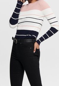 Pull en maille côtelée à rayures rose, blanches et bleu marine. Associé à un jean noir et une ceinture cloutée. Manches longues et col rond.