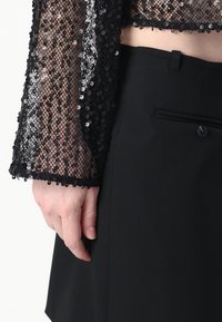 Čierny top s flitrami a krátkymi priesvitnými rukávmi, skombinovaný s čiernymi nohavicami s vysokým pásom, ktoré majú bočnú kapsu a detail gombíka.
