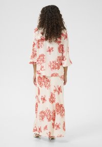 Floral two-piece outfit featuring a cream base with large red flower patterns. Loose-fitting top with elbow-length sleeves and a long skirt.