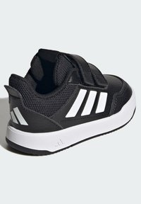Crna sportska cipela s teksturiranim sintetičkim gornjim dijelom, Velcro remenom, bijelim uzorkom s tri pruge i laganim bijelim gumenim potplatom.