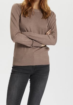 Maglione a maglia marrone chiaro con maniche lunghe, polsini e orlo a costine, caratterizzato da una consistenza morbida e un classico scollo rotondo. Indossato con jeans neri.