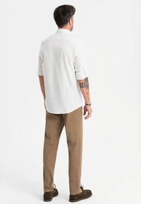 Chemise à manches longues à rayures blanches avec des poignets retroussés, associée à un pantalon beige clair et des chaussures foncées. Présente un design décontracté et une coupe confortable.