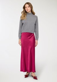 Maglione grigio corto con collo alto abbinato a una lunga gonna di raso fucsia lucido. L'outfit è completato da tacchi rossi con fiocchi.