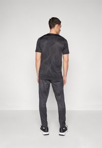 Zwart sportoutfit bestaande uit een T-shirt met korte mouwen met een geometrisch patroon en bijpassende broek. De stof lijkt lichtgewicht met een gladde textuur.